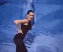 a woman in a black dress is dancing on a stage in front of a blue wall .