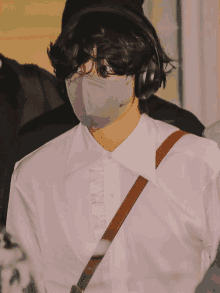 a man wearing a face mask and headphones has a white shirt with a brown strap around his shoulder