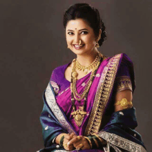 a woman wearing a purple saree and gold jewelry smiles