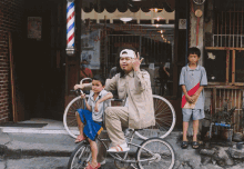 a man sits on a bike with two children in front of a barber shop with a sign that says no smoking