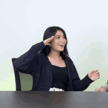 a woman in a black top and black cardigan salutes