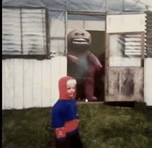 a little boy in a red hoodie stands in front of a building with a stuffed animal in the doorway