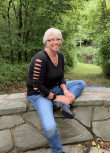 a woman sits on a stone wall in front of trees