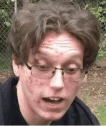 a close up of a young man wearing glasses and a black shirt .