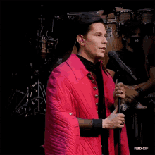 a man in a red jacket singing into a microphone with rbd.gif below him