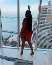 a woman in a red dress stands in front of a window with a bank of america building behind her