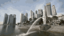 a statue of a lion is spraying water in front of a skyline with a building in the background that says one world