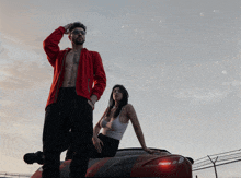 a man in a red jacket stands next to a woman in a white tank top