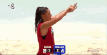 a woman in a red shirt is standing on a beach with her arms outstretched in front of the ocean .