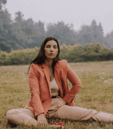 a woman in an orange blazer sits on the grass