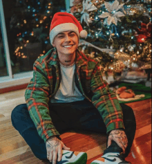 a man wearing a santa hat is sitting on the floor in front of a christmas tree