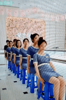 a row of women sitting on blue stools in front of a sign that says ' beauty ' on it