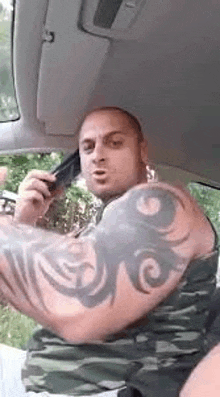 a man with a tattoo on his arm is talking on a cell phone while driving a car .