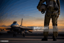 a pilot is standing in front of a fighter jet and holding his helmet