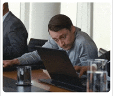 a man sits at a table with a laptop and a glass of water