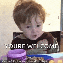 a little boy is sitting at a table with a plate of food and a cup that says youre welcome .