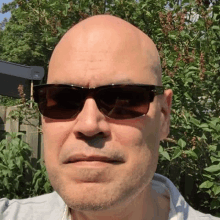 a bald man wearing sunglasses is taking a selfie in front of a fence .