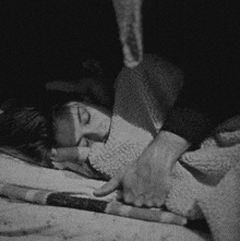 a black and white photo of a woman sleeping on a bed with a man holding her hand .