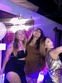 three women are posing for a picture in front of a purple curtain