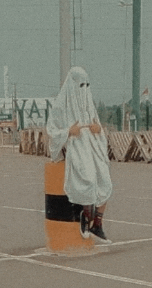 a person in a ghost costume is sitting on top of a barrel in a parking lot .