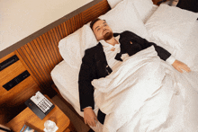 a man in a suit is laying on a bed next to a telephone