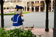 donald duck standing in front of a sign that says " happy disneyland "