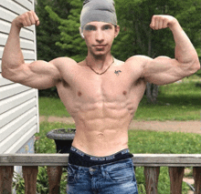 a shirtless man flexes his muscles in front of a white house wearing mountain ridge underwear