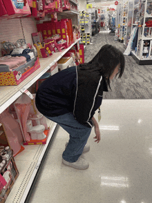 a girl is squatting down in front of a shelf with a doll on it