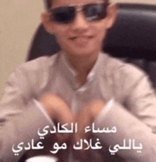 a boy wearing sunglasses is sitting in a chair with arabic writing behind him