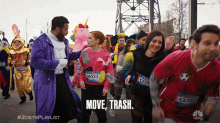 a man in a purple robe talks to a woman in a pink sweater who is wearing a unicorn shirt