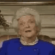 an elderly woman in a blue jacket and pearl necklace is sitting in a chair .