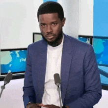 a man in a blue suit and white shirt is standing in front of a microphone in a news studio .