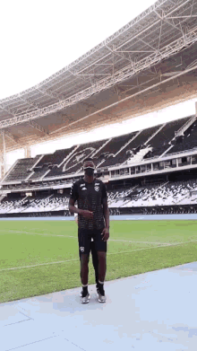 a man stands on a soccer field in front of an empty stadium that says ' atletico ' on it