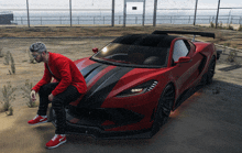 a man in a red shirt sits on the front of a red sports car