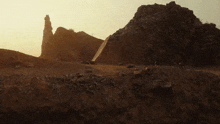 a large rock formation in the middle of a desert with a pyramid in the distance .