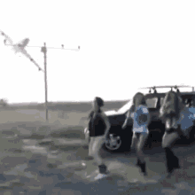 a group of girls are dancing in front of a car while a kite is flying in the sky .