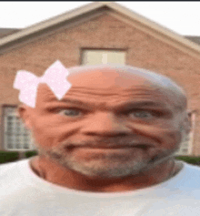 a bald man with a beard and a pink bow on his head is standing in front of a brick house .