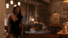 a woman in a black dress is standing in a living room with a couch .