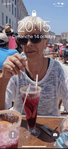 a phone screen shows a woman sitting at a table drinking from a glass with a straw