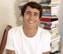 a young man smiles in front of a stack of books including one by t.c. boyle and a stack of other books