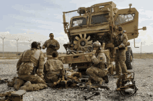 a group of soldiers are kneeling in front of a military vehicle with a fan on the front