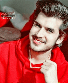 a man wearing a red hoodie and a necklace is smiling for the camera