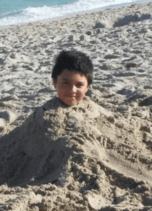 a young boy is buried in sand on the beach