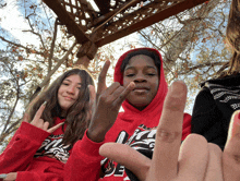 a boy wearing a red hoodie with the letter l on it is giving the middle finger