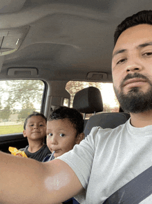 a man with a beard is driving a car with two children