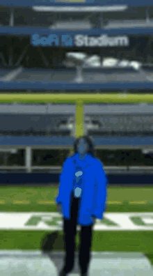 a man in a blue jacket is standing on a football field in front of a sign that says stadium