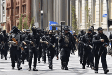 a group of men with guns march down a street with a sign that says ' a ' on it in the background