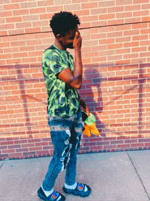 a man wearing a green tie dye shirt covering his face while standing in front of a brick wall