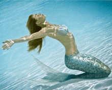 a woman in a mermaid costume is kneeling down in the water with her arms outstretched