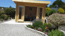 a wooden house with a clock on the wall sits in the middle of a garden